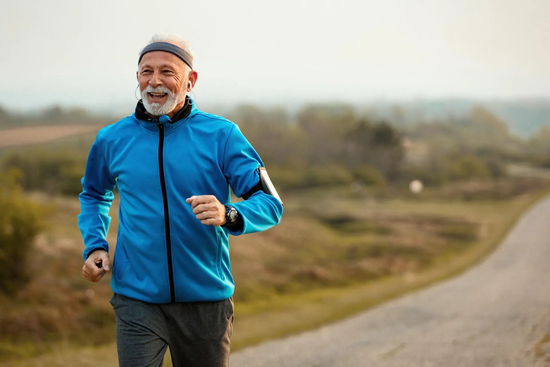 Äldre man joggar leende på en väg i höstlandskap